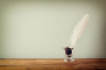photo of white Feather and inkwell on old wooden table. retro filtered image
