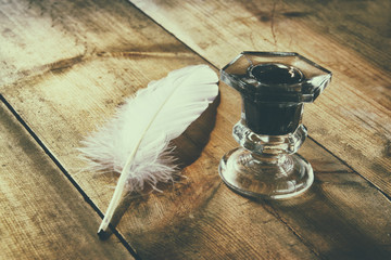 photo of white Feather and inkwell on old wooden table. retro filtered image
