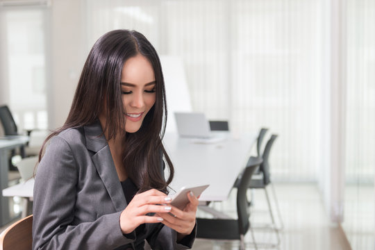 Asian business woman with smart phone and checking her email texting, messaging, using smartphone application with touch screen technology in office, business concept.