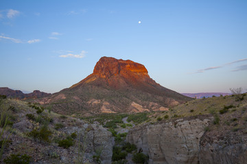 Naklejka na ściany i meble Cerro Castellan at sunrise is viewed with Tuff Canyon in the foreground. The moon is still visible in the sky. The picture is taken in Big Bend National Park.