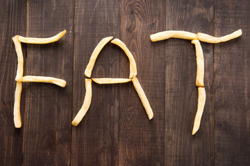 French fries forming word fat on wooden background