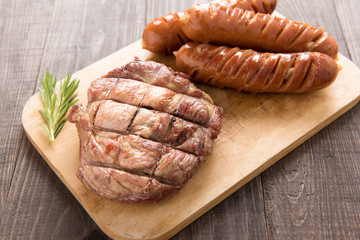 Grilled steak and sausage on a wooden background