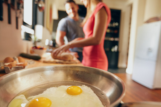Fried eggs in a pan with couple standing in background