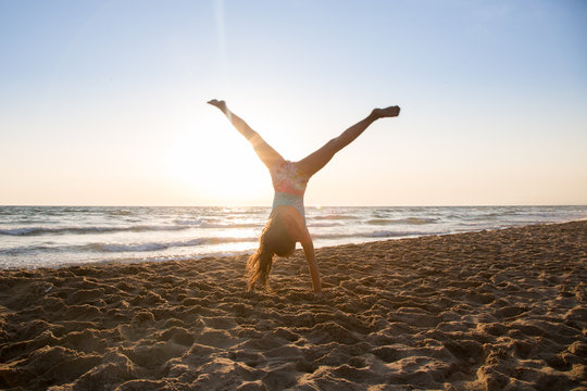 Bambina che fa la ruota sulla spiaggia in controluce