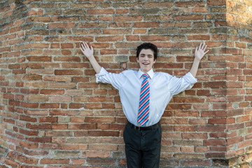 Handsome boy raising arms in front of a brick wall