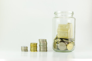 Stacked Malaysian Ringgit coins leading to miniature dream house inside glass jar, isolated on white background