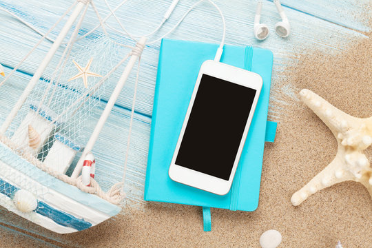 Smartphone and notepad on sea sand with starfish and toy boat