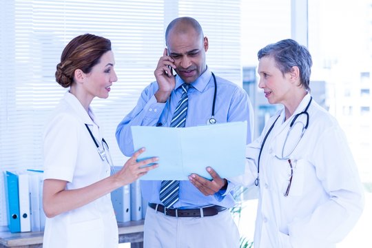 Concentrated doctor showing file to his colleagues while calling