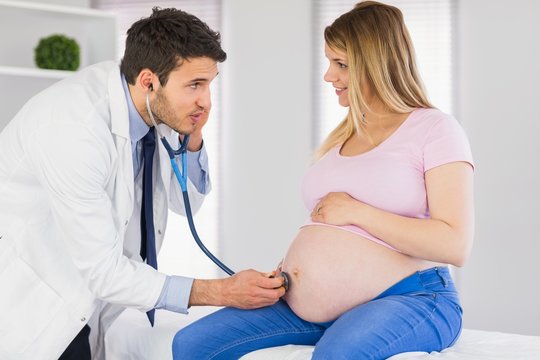 Doctor talking to pregnant patient while examining her stomach