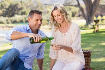 Smiling couple sitting and pouring wine in glass 