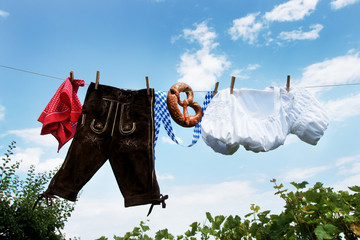 Oktoberfest, Volksfest - Lederhose, Dirndl und Breze hängen an Leine vor weiß-blauem Himmel
