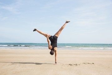 Fototapeta na wymiar Fit woman cartwheeling on the sand