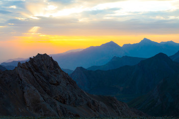 Sunset mountain panorama.  Silhouettes of highland ridges and peaks of warm and cool tones visible perspective distance luminous sun setting on background © alexbrylovhk