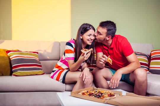 Funky Young Couple Eating Pizza On A Couch