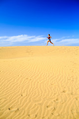 Fototapeta na wymiar Young woman running on sand desert dunes