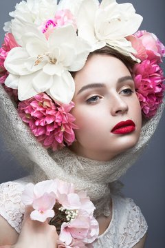 Beautiful girl in a headscarf in the Russian style, with flowers on the head and red lips. Beauty face. Picture taken in the studio on a gray background.