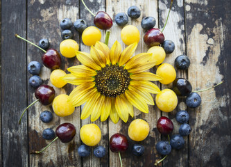fresh different berries on a wooden background with sunflower, top view