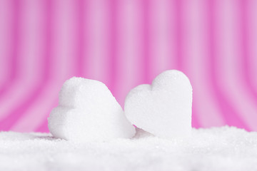 Two white sugar hearts in pile of sugar on pink striped background.