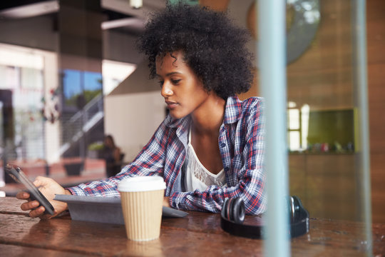 Businesswoman On Phone Using Digital Tablet In Coffee Shop