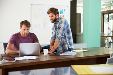 Two Businessmen Working On Laptop In Office Together