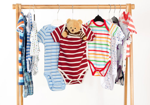 Dressing closet with clothes arranged on hangers.Colorful onesie of newborn,kids, toddlers, babies on a rack.Many colorful t-shirts, shirts,blouses, onesie hanging, bear toy