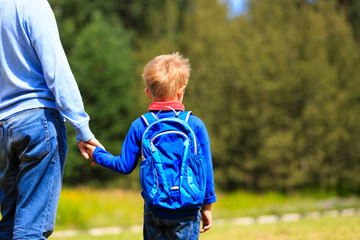 father holding hand of little son with backpack outdoors