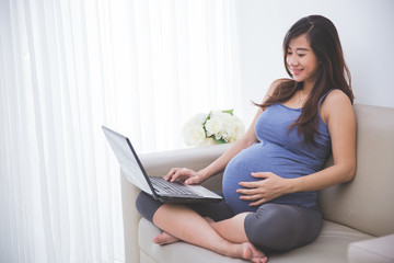 Naklejka premium Beautiful pregnant woman checking a laptop pc while sitting on t