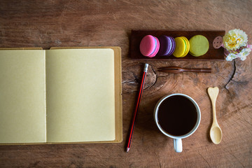 Colorful macaroons and a cup of coffee with blank notebook on wooden table