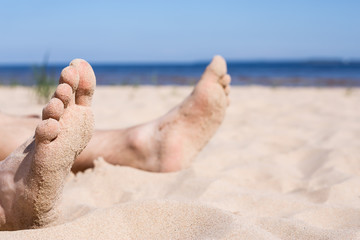 Relax on a deserted beach - sunbathing. Men's foot stained in the sand against the blue sky and the sea