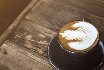A cup of coffee latte on wood table with orange flare and soft light