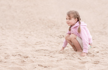 little girl kneeling on the sand and looking ahead