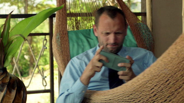 Focused businessman playing game on smartphone while lying on hammock 
