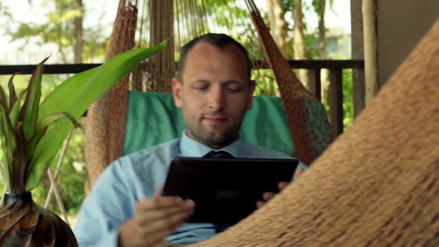 Young businessman with tablet computer lying on hammock on terrace 

