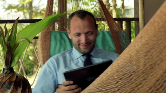 Happy businessman playing game on tablet computer while lying on hammock 
