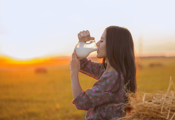Fototapeta na wymiar Young woman drinking milk from the jug at sunset