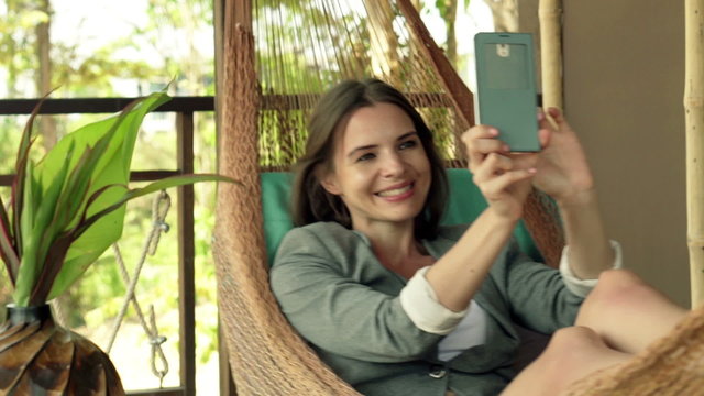 Young, pretty businesswoman taking selfie with cellphone lying on hammock
