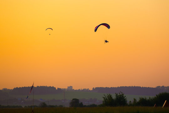 silhouette of a paraglider with a motor in the orange sunset