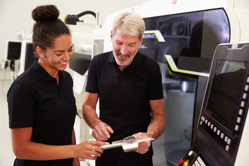 Female Apprentice Working With Engineer On CNC Machinery