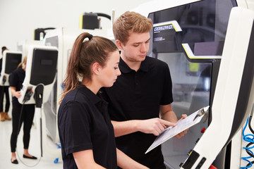 Two Young Engineers Operating CNC Machinery On Factory Floor