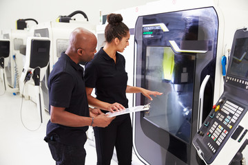 Female Apprentice Working With Engineer On CNC Machinery