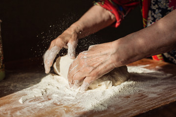 Senior woman hands knead dough on a table in her home kitchen
