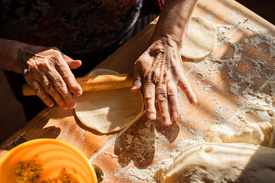 Senior woman hands rolling out dough in flour with rolling pin in her home kitchen