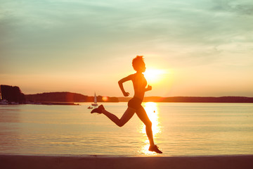 Attractive young African girl athlete running at sunset along the beach. Fitness training of runner.