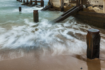 Waves breaking on beach and groynes in evening light. Seaton Sluice Northumberland, England. UK.