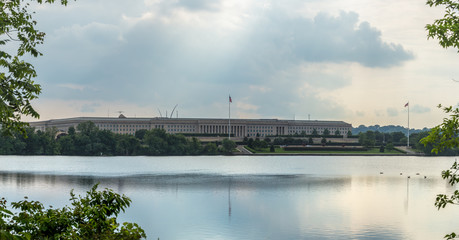 The Pentagon, headquarters of the Department of Defense, behind and reflected in the Pentagon Lagoon Yacht Basin with storm clouds developing in the sky  and the sun's rays peeking through.