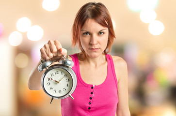 Serious redhead girl holding a clock over white background