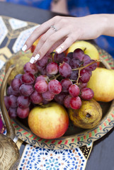 Young woman is holding fresh grapes near the salver with apple, pear