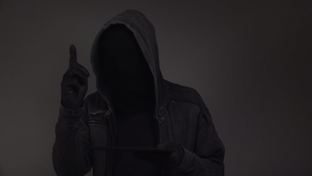 Cyber crime threat, unrecognizable faceless hooded cyber criminal using digital tablet computer to access internet web page, p2p and piracy concept, 4k uhd footage