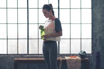 Fit woman standing in profile in loft gym holding water bottle