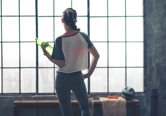 Rear view of woman looking out of loft gym holding water bottle